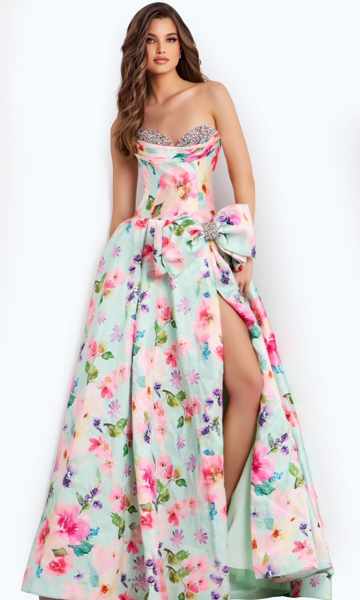 A woman poses against a plain light background in the Jovani 49197 Long Prom Dress in Mint/Multi, featuring a strapless floral A-line design with sweetheart neckline, jeweled corset bodice, high slit, and large bow at the waist.